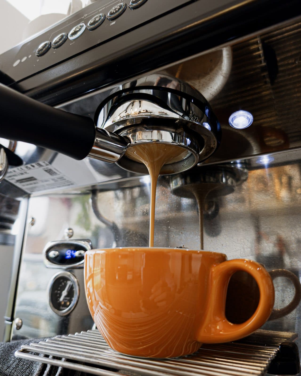 An espresso pours into an orange cup